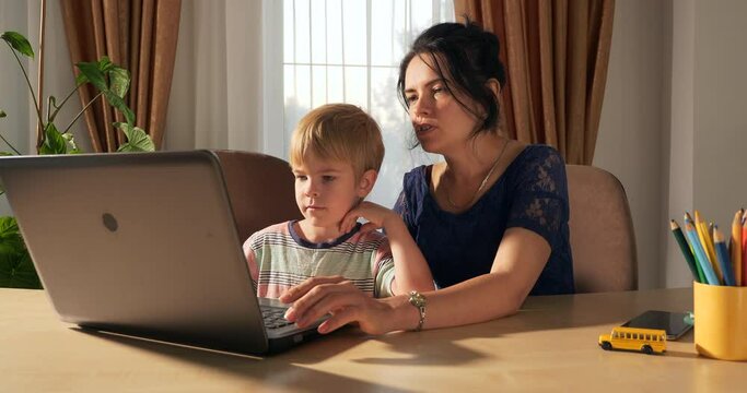 Mother Teach Child Study Online Using Laptop Computer. Little Boy Distance Learning at Home. Preschooler Kid Sits at Desk Table in Room Near Window 4K