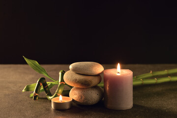 Spa stones with burning candle and bamboo branch on table against black background