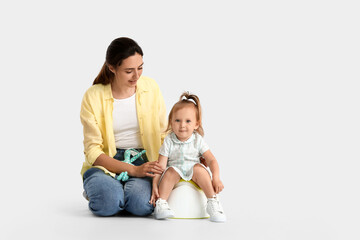 Mother potty training her little daughter on light background
