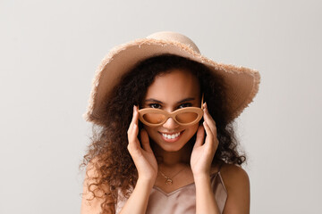 Beautiful African-American woman in broad brim hat on light background