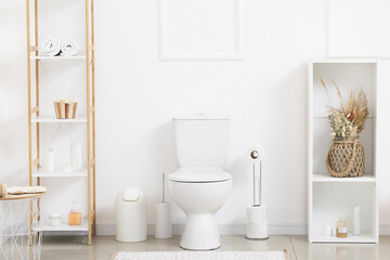 Fototapeta na wymiar Interior of light restroom with toilet bowl, paper holder and shelf units