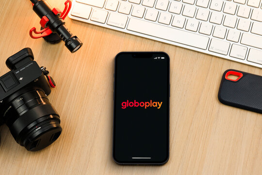 Globoplay app on smartphone iPhone 13 Pro screen on wooden table. Content creator environment with keyboard, camera and mic. Rio de Janeiro, RJ, Brazil. November 2021