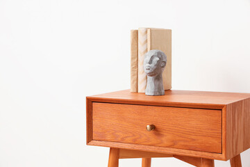 Wooden bedside table with books and decor near light wall