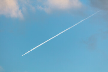 Airplane trail on a blue sky with clouds. Background