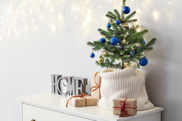 Small Christmas tree with gifts and clock on shelf near light wall