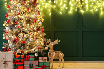 Beautiful Christmas tree with glowing lights, gifts and wooden reindeer near green wall