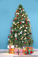 Fototapeta na wymiar Beautiful decorated Christmas tree and gift boxes near blue wall