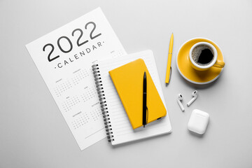 Paper calendar for year 2022, stationery supplies, earphones and cup of coffee on grey background