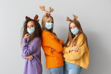 Beautiful young women in medical masks and with Christmas decor on light background