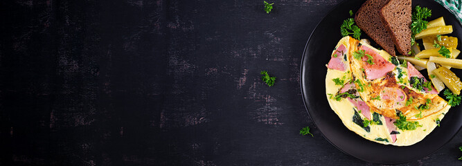 Omelet with boiled sausage and herbs, served with fermented cucumbers and bread. Rustic cuisine. Omelette. Top view, banner