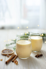 Two glasses of eggnog on a white wooden table by the window. Christmas dessert. Sweet winter cocktail. Vertical photo Selective focus
