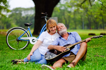 happy two caucasian elderly in park and playing guitar