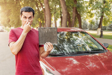 Frustrated car driver with an allergy to dust collected in an old dirty ventilation filter. Polluted air in the cabin