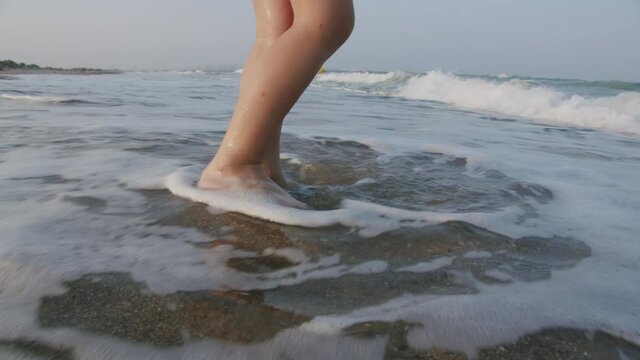 Close up shot of kid's feet standing in the sand with ocean waves gently rolling in during the sunset