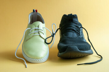 Male and female shoes linked on a yellow background. Concept-relationship between a man and a woman. Equality. Leather shoes. Men's trainer.