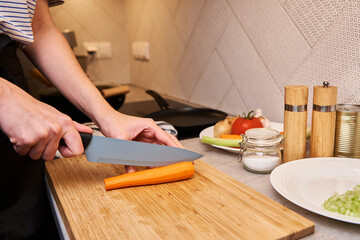 Woman with knife cuts fresh carrot slices for cooking