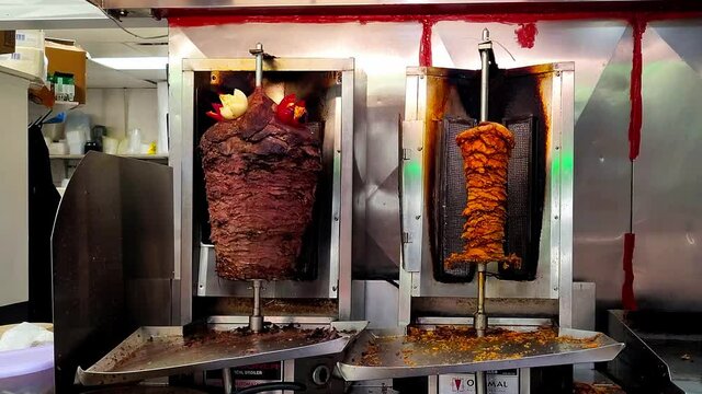 4k shawarma rotating upright on slow roasting vertical BBQ left its beef slices with decorative cut onions and tomatoes on the top, and onto the right its marinated chicken breast pieces on the spit.