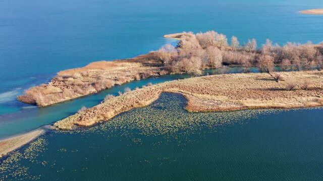 River mouth - landform caused by sediment deposition where stream Ljuca flows into lake Plav water in Montenegro. Peninsula or promontory split into two halves under a hill or mountain.