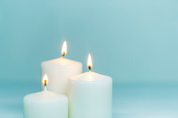 Fototapeta na wymiar Three white candles burning on white gradient background. Front view. Horizontal composition. Set of white candles over blue background with copy space