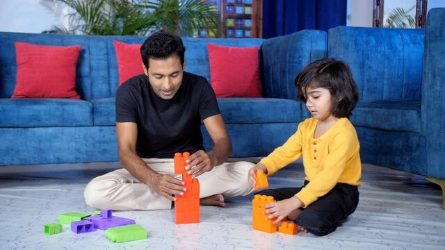 A middle-aged father and his young son playing with building blocks. A carefree dad and a sweet little kid sitting together on the floor in the living room - a leisure activity  family bonding  dev...