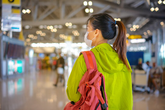 Asian female with face mask is carrying a backpack in airport terminal.