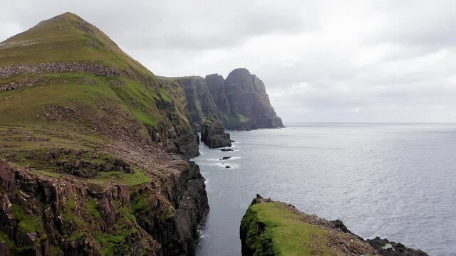 Aerial back view of huge cliffs in faroe islands, green rocky mountain,powerful ocean waves,in a cloudy summer day,green meadow and rock in wild nature,wild no house.