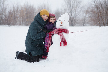 Fototapeta na wymiar grandmother with a small granddaughter make a creative snowman and play in nature in winter. family spends time together in winter in nature