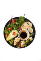 Vegan snack plate with hummus, avocado, tomato, salad, cauliflower and broccoli, ciabatta bread, oil and 
balsamic vinegar sauce on a black plate. Isolated on white, top view.