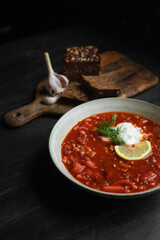 Vegan bean borsch with sour cream, garlic and grain bread on a wooden boad in the background. Black wooden background.