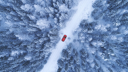 Country road going through the beautiful snow covered forest. Red car driving on winter road. Aerial view. Drone photography. - 470807473