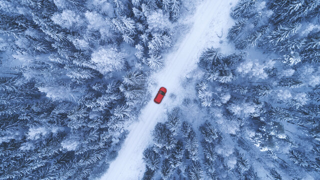 Country road going through the beautiful snow covered forest. Red car driving on winter road. Aerial view. Drone photography.