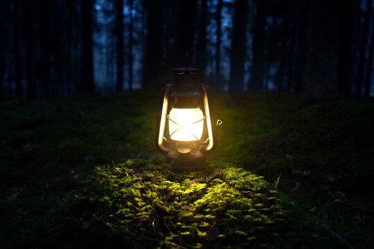 Vintage old lantern lighting in the dark forest. Travel camping concept.  Burning lantern on a moss at forest in the night. Stock Photo