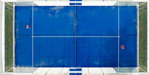 View from above, stunning aerial view of two people playing on a blue padel court. Padel is a mix...