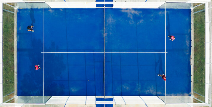 View from above, stunning aerial view of some people playing on a blue padel court. Padel is a mix between Tennis and Squash. It's usually played in doubles on an enclosed court.