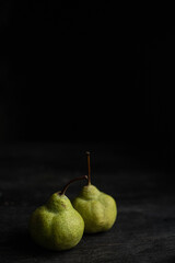 Two ripe green pears on black wooden desk, black background.
