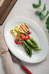 Grilled asparagus with tomatoes and herbs on a white plate. Vegan dish with vegetables and asparagus, top view