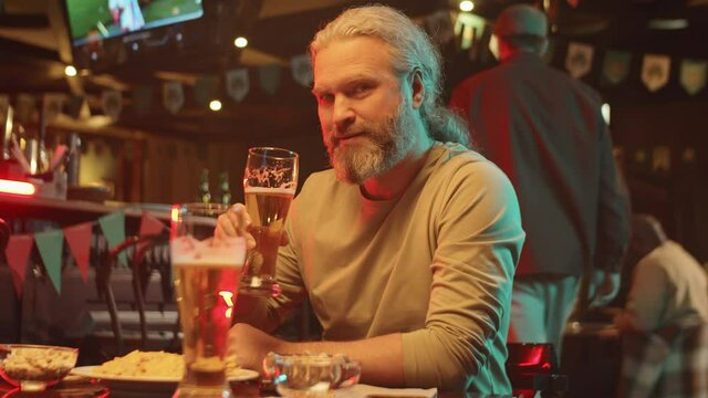 Slow motion shot handsome mature bearded man with long hair wearing casual clothes spending time in pub drinking ale