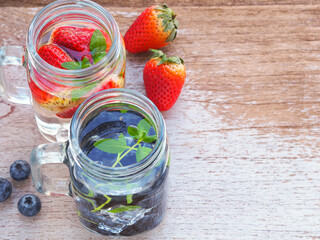 Infused water with fresh organic blueberries and strawberry on rustic wooden background. Space for your text.