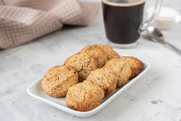 Oatmeal cookies on a white rectangular plate on the table with a glass cup of black coffee and kitchen utensils horizontal photo