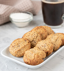 Oatmeal cookies on a white rectangular plate close-up on the background of a cup of black coffee and sugar