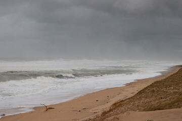 The beach on a stormy day. The waves break towards the beach, the ocean is raging, the sky is very dark and threatening. the beach has practically disappeared.