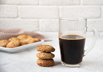 A stack of oatmeal cookies and a glass mug with black coffee are on the table with cookies and a towel