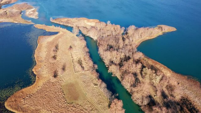 River mouth - landform caused by sediment deposition where stream Ljuca flows into lake Plav water in Montenegro. Peninsula or promontory split into two halves. Aerial drone view on a sunny day.