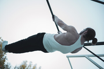 a red-haired boy with a ponytail doing calisthenics in a park.