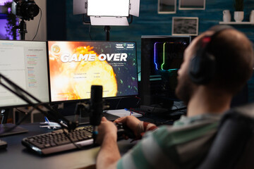 Man streaming video games with microphone and losing on computer. Gamer looking at monitors with live stream chat and online game, playing and broadcasting gameplay with headphones.