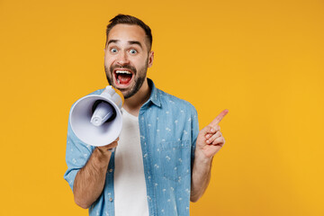 Young expressive happy man 20s wearing blue shirt white t-shirt hold scream in megaphone announces discounts sale Hurry up point finger aside on workspace isolated on plain yellow background studio. - obrazy, fototapety, plakaty