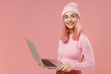 Young smiling woman 20s with bright dyed rose hair in rosy top shirt hat hold use work on laptop pc...