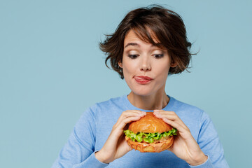 Young wistful caucasian fun cool woman 20s wear casual sweater biting eating burger lick lips...