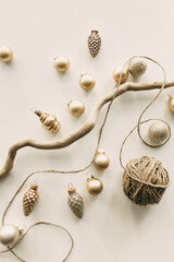 Stylish New Year mood decoration with wooden branch and wrapping rope surrounded with tiny golden balls and artificial glittered pine cones on white surface imitating Christmas postcard. Xmas mockup