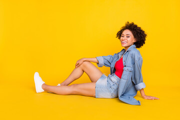 Photo of lovely lady sit floor enjoy rest wear denim jacket mini skirt sneakers isolated yellow...